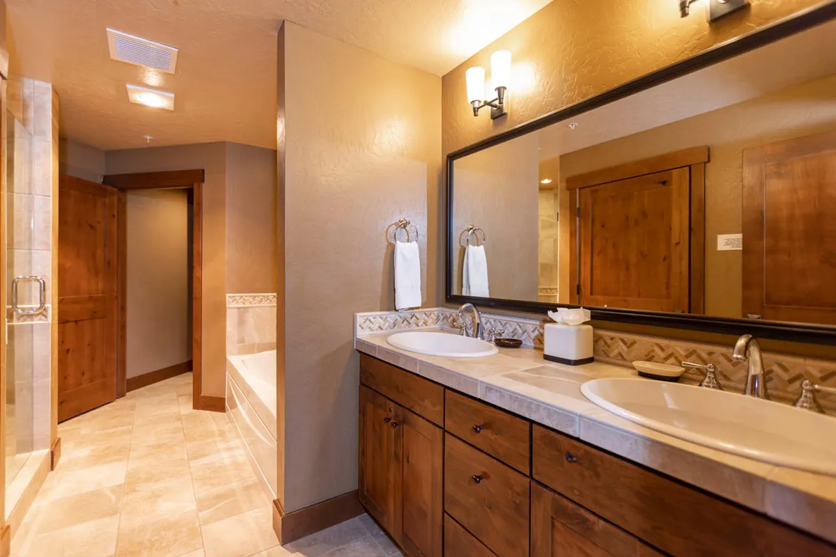 A serene bathroom with a double sink vanity, large mirror, warm wooden cabinetry, and a bathtub. The setting is calm and conducive to relaxation, ideal for spa-like routines.