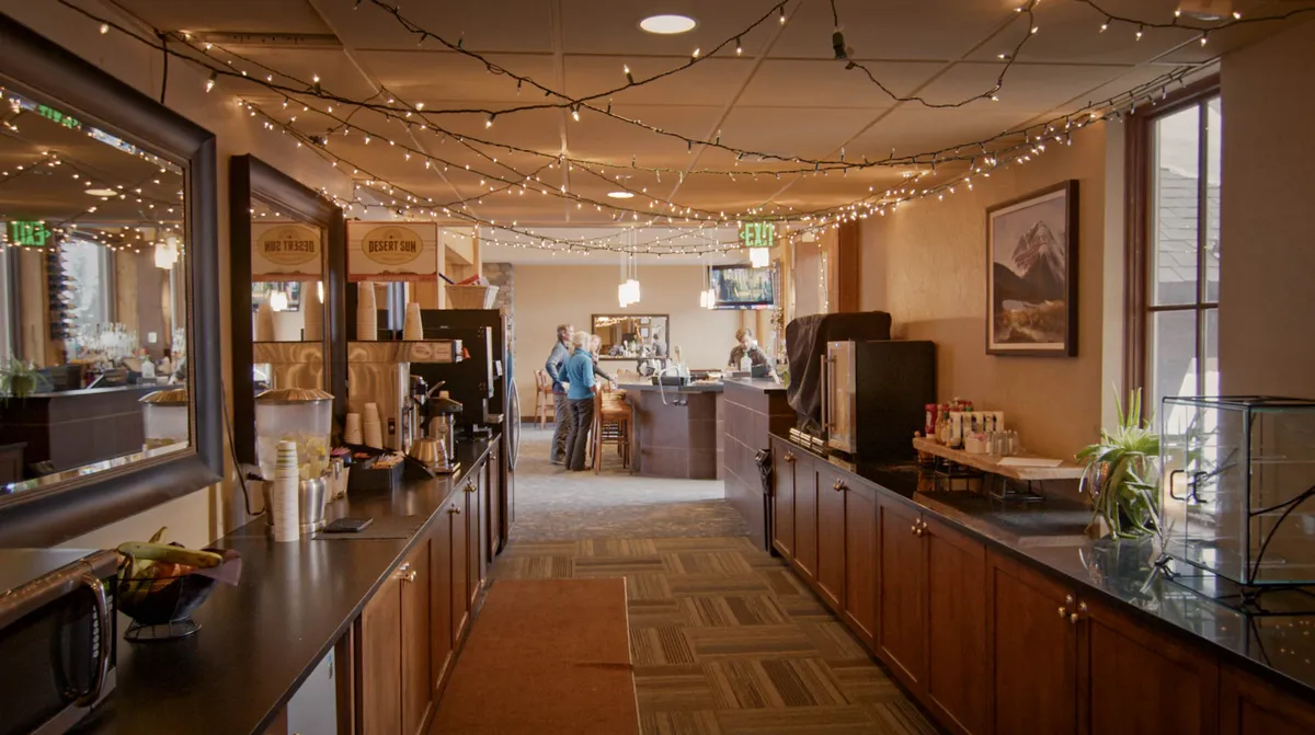 A welcoming living and dining area with a coffee station, comfortable seating, decorative lights, and artwork, inviting guests to relax and socialize. The space exudes warmth, perfect for gathering after a day outdoors.