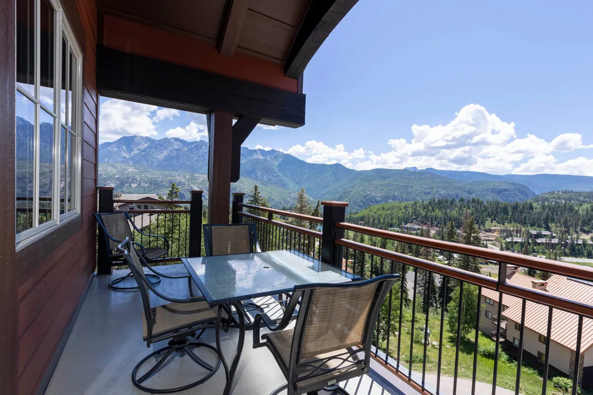 The image showcases the condo's spacious outdoor dining area, set against a breathtaking backdrop of mountains. Sunlight gently bathes the space, inviting guests to relax, dine, and soak in panoramic alpine views from the comfort of the private balcony. The tranquil setting hints at mornings spent watching the sunrise, evenings of stargazing, and the possibility of spotting local wildlife from this prime vantage point.
