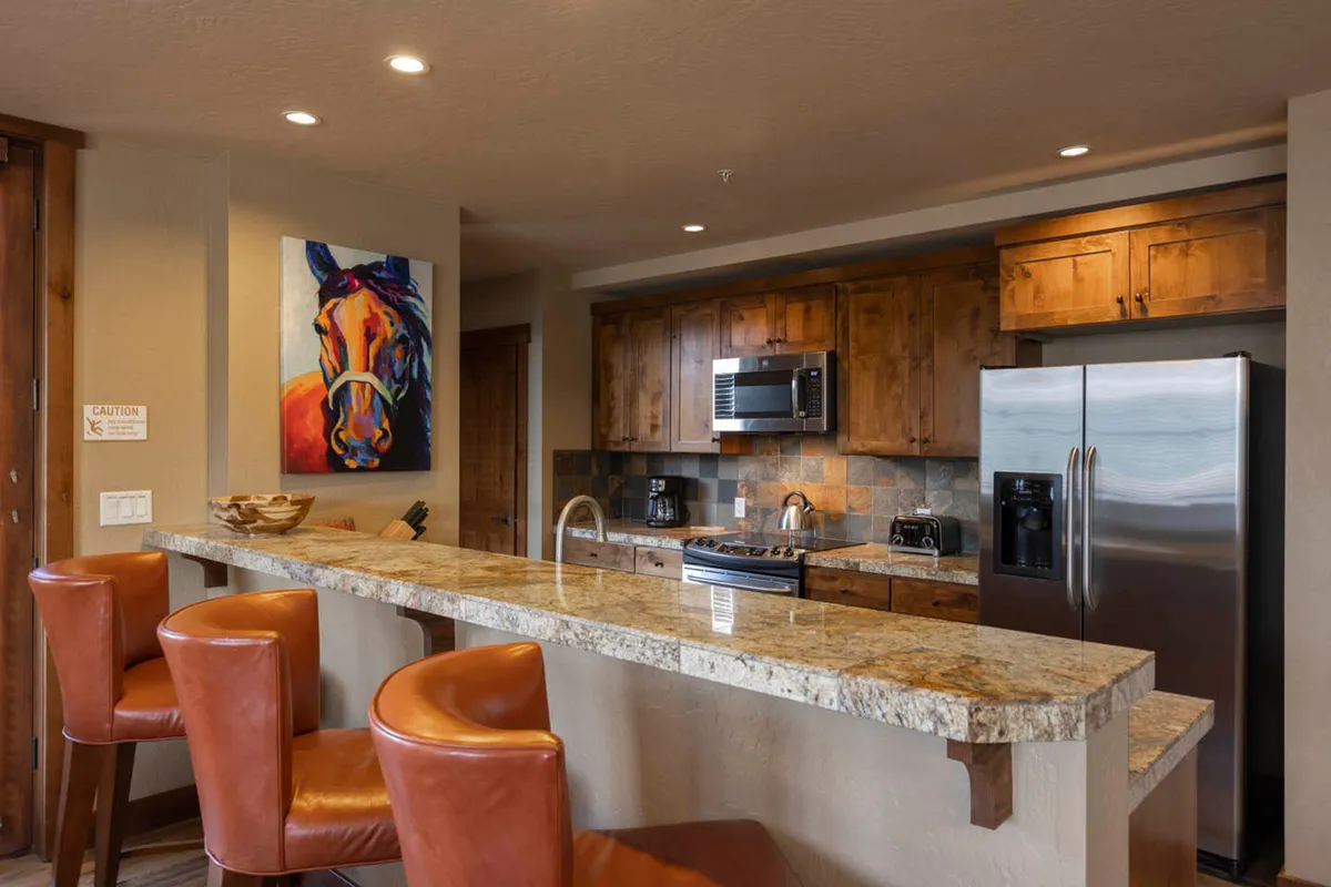 A modern open kitchen with granite countertops, stainless steel appliances, bar stools, and tasteful art. The layout suggests a space designed for both cooking and socializing, with elegant finishes that elevate the cooking experience.
