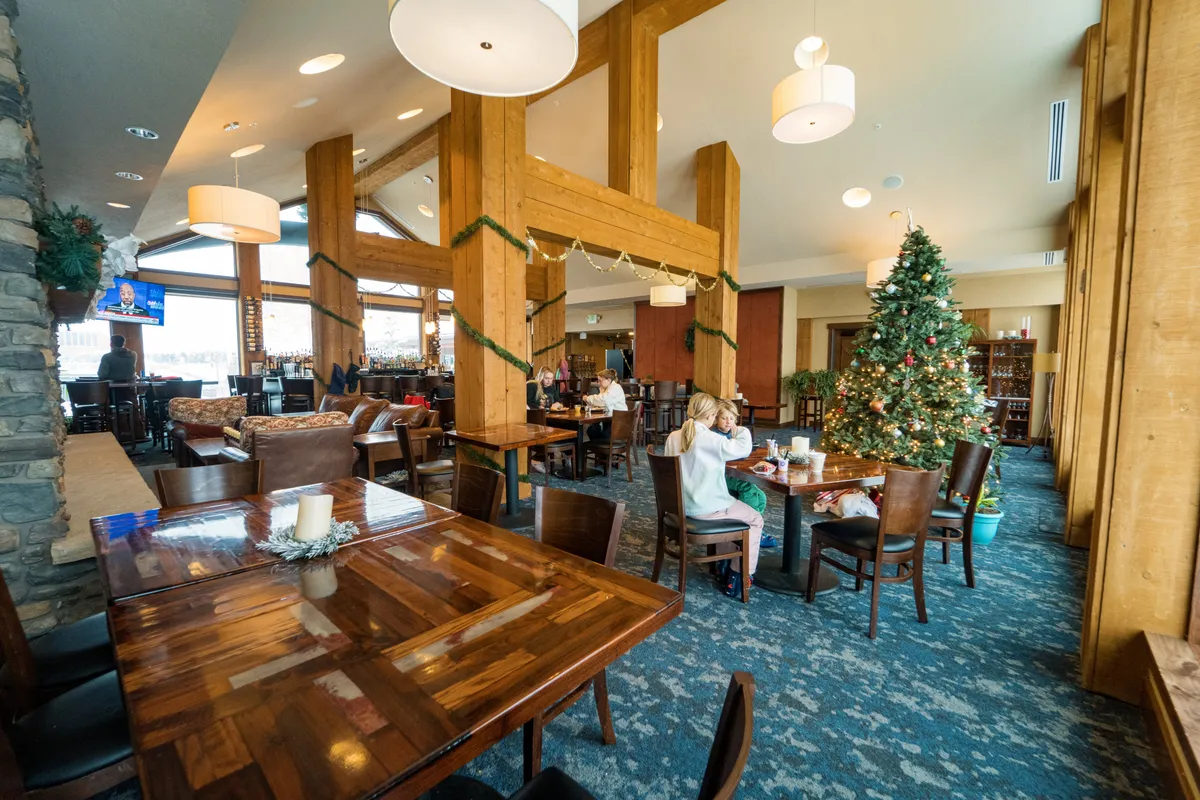 A cozy, timber-framed restaurant interior filled with natural light, décor for the holidays, and groups of people enjoying meals at wooden tables. The festive, inviting atmosphere supports social gatherings and family dining.